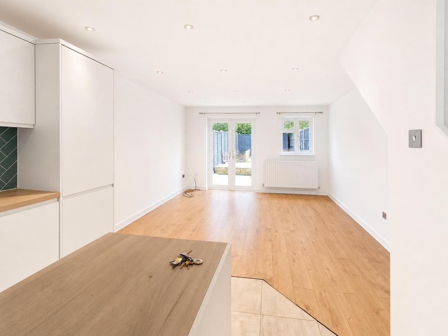 Open-plan kitchen and living space with white walls and ceiling, white skirting boards, wooden flooring and built-in cabinetry.