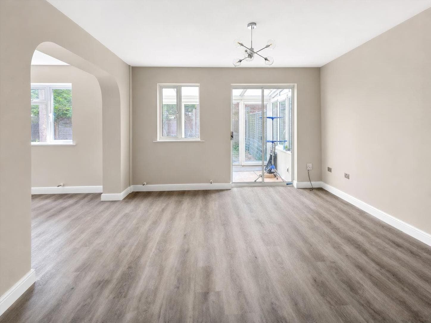 Open-plan living space with neutral painted walls, white ceiling and skirting boards, windows and glazed doors to garden