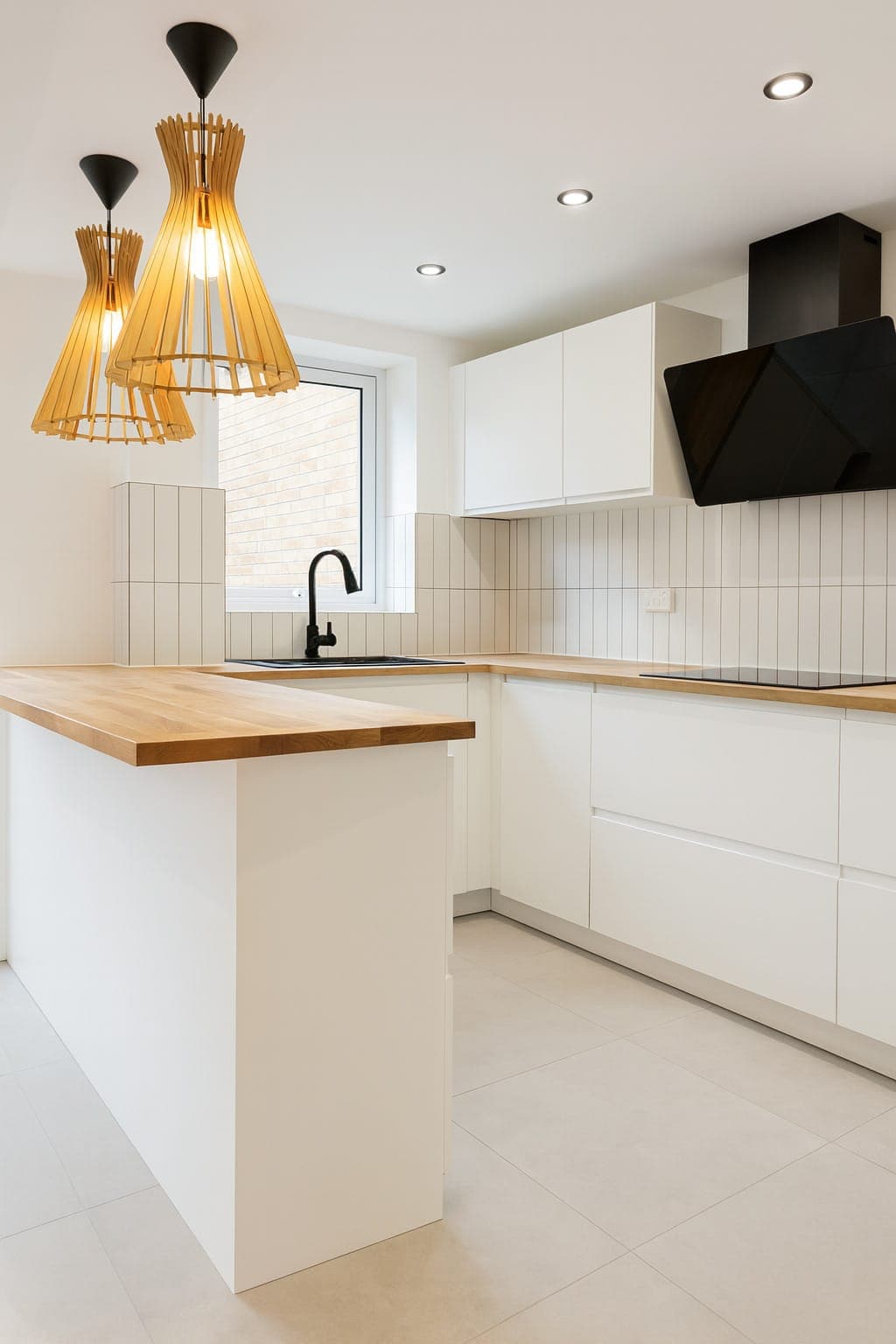 Kitchen with white painted cabinets, cream walls, recessed ceiling lights, timber panelling to half-height, island with wood worktop and black tap.