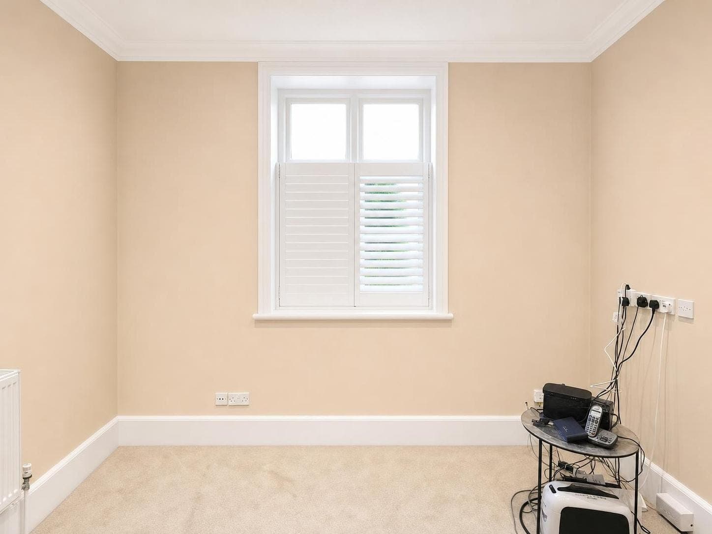 Bedroom with pale peach walls, white ceiling, white skirting boards and window frame with shutters.