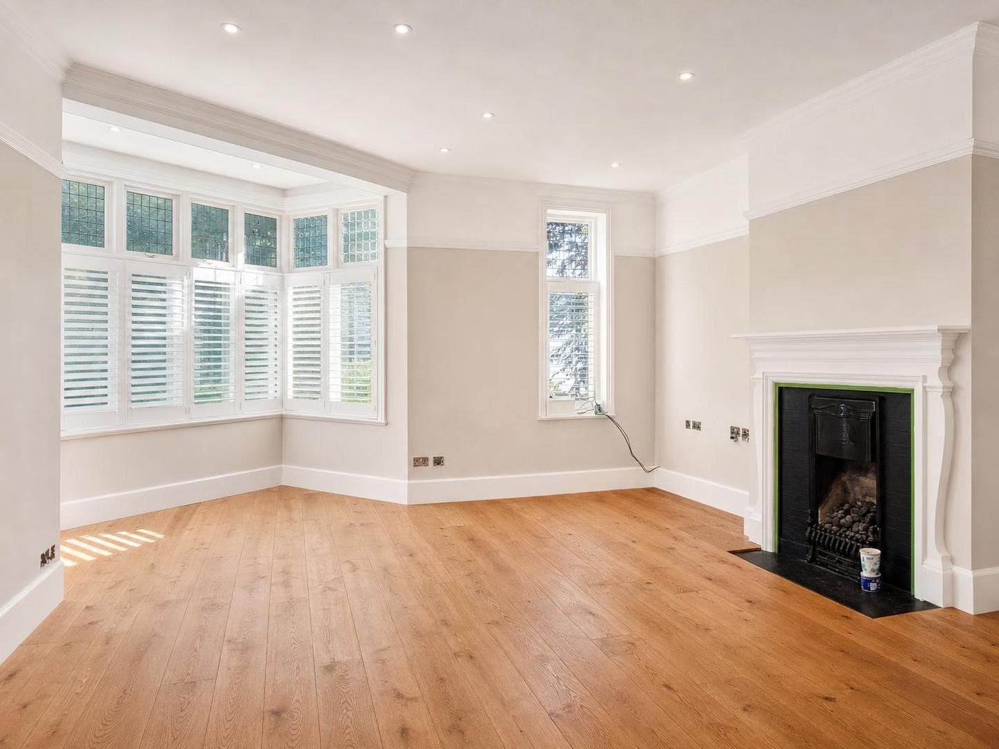 Living room with pale neutral walls, white skirting boards, architrave detail around a fireplace opening, and white ceiling with recessed lights