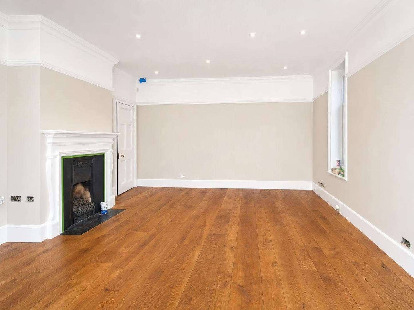 Living room with pale neutral walls, white dado rail, skirting boards and fireplace surround, wooden floor, recessed ceiling lights