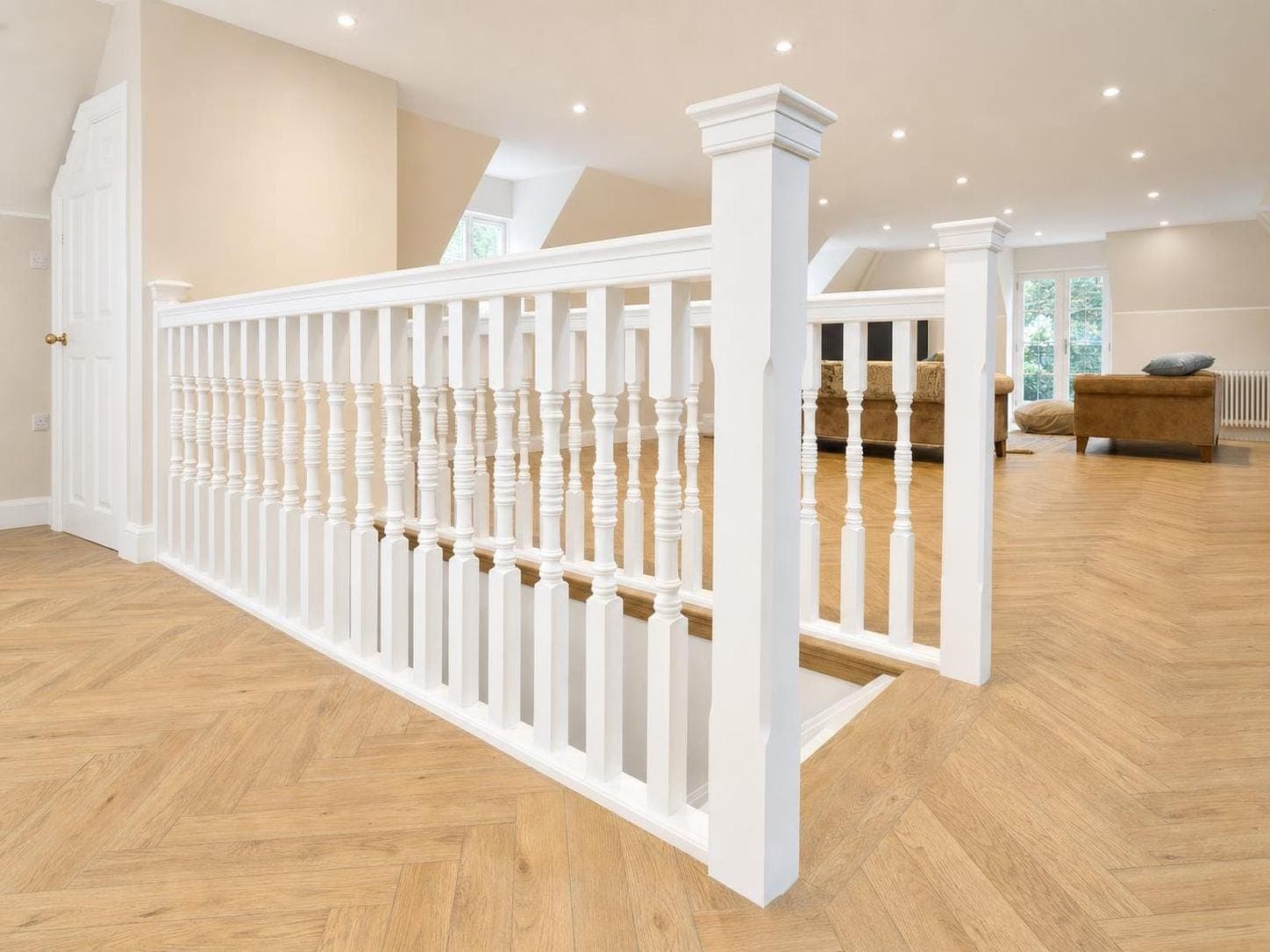 After: Landing with white painted staircase balustrade, newel posts and handrail, with cream walls and recessed lighting.
