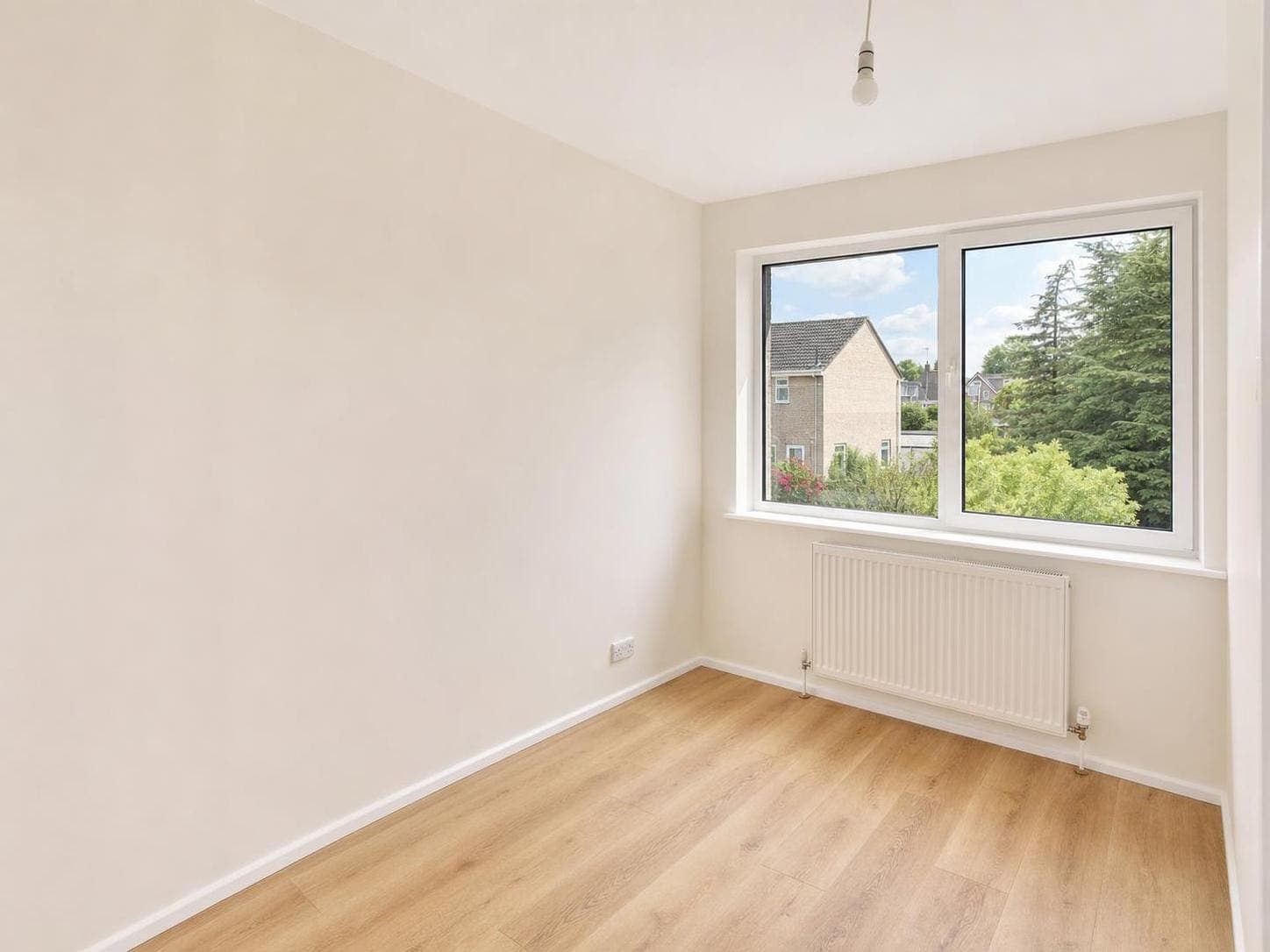 Bedroom with pale cream walls and white ceiling, white skirting boards and window frame, large window overlooking garden.
