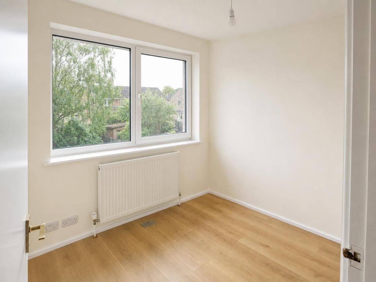 Bedroom with emulsion-painted walls and ceiling in warm beige, white window frame, radiator and wooden floor