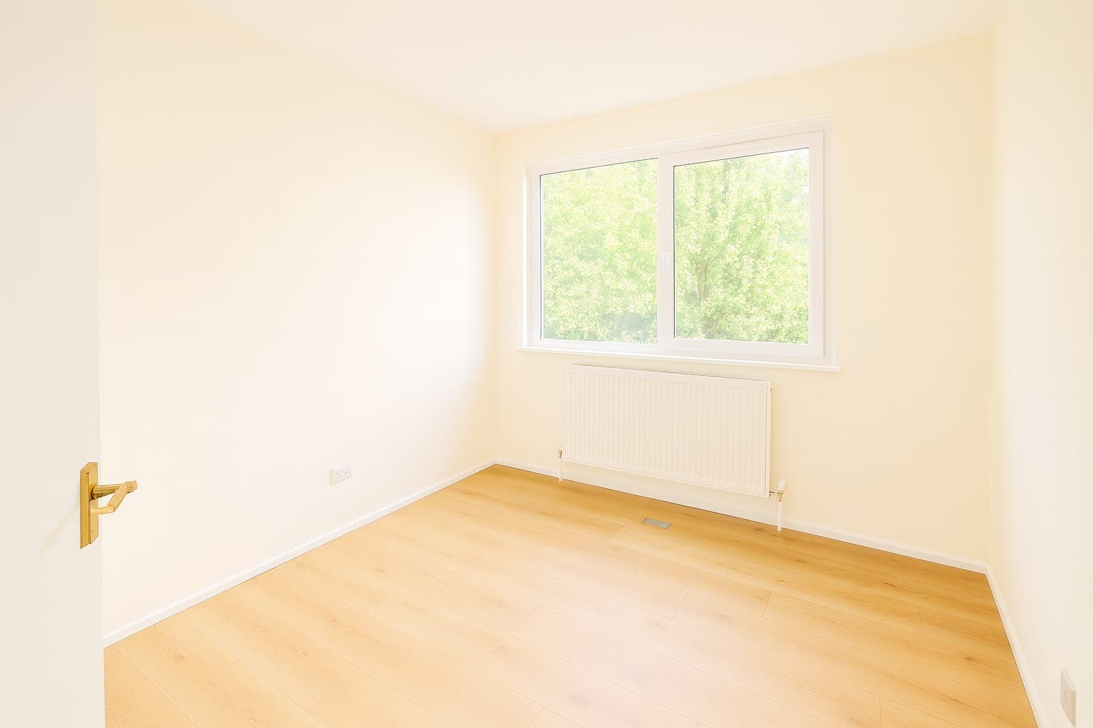 Bedroom with cream-painted walls and white skirting boards, double window with white frame, wooden floor and radiator.
