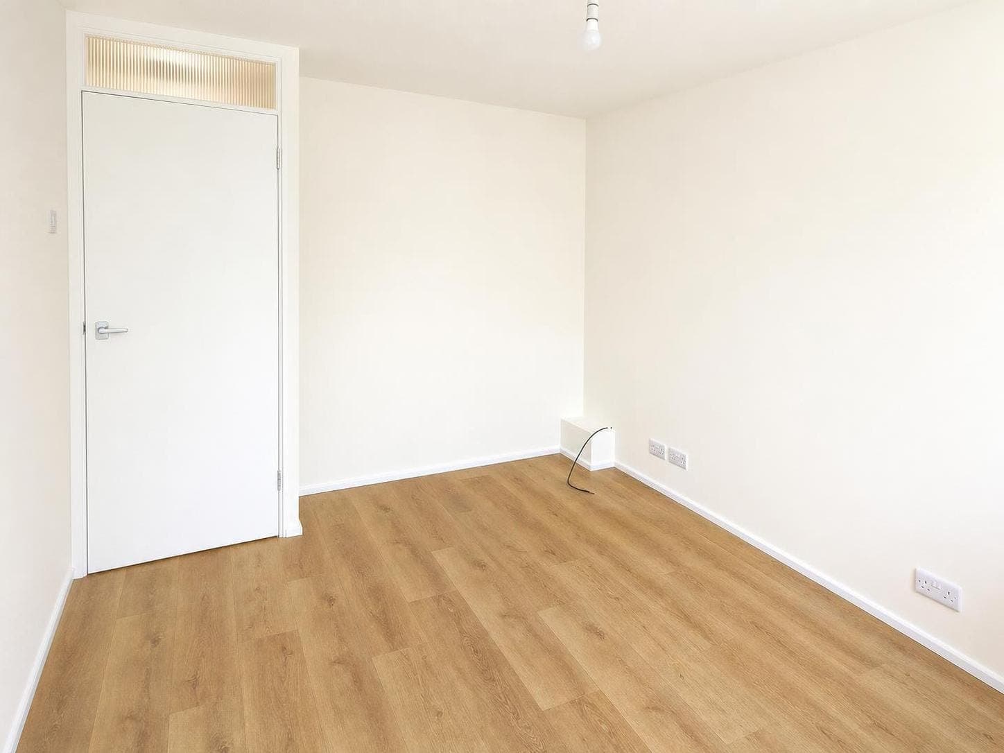 Bedroom with white painted walls, white door frame and skirting board, and modern light pendant.